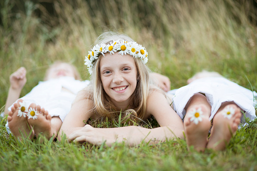 Cute smiling girl in the Ukrainian national wear on the green meadow. Portrait of fun happy girl with flowers, sitting on the green grass.