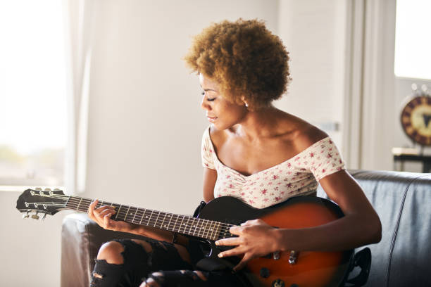 donna afroamericana che suona la chitarra a casa - afro americano foto e immagini stock