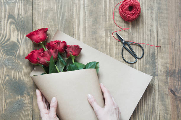 istock Wrapping a red roses bouquet on wooden table. View from above. Rustic style. Top view. 932549206