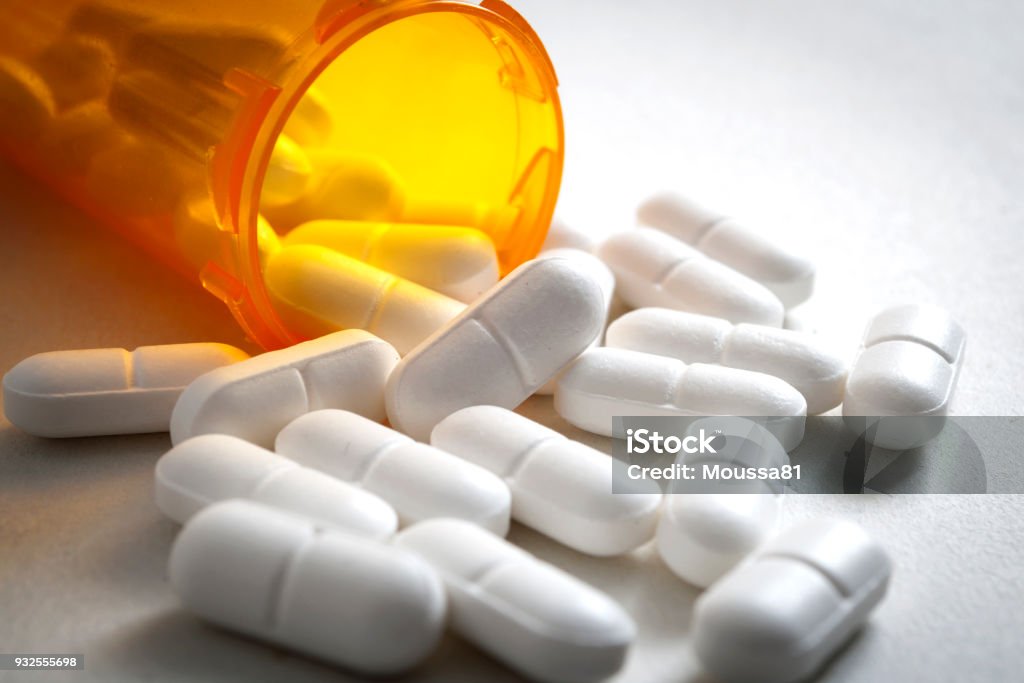 hydrocodone is an analgesic prescribed as potent pain medication Opioid epidemic, painkillers and drug abuse concept with close up on a bottle of prescription drugs and hydrocodone pills falling out of it on white Medicine Stock Photo