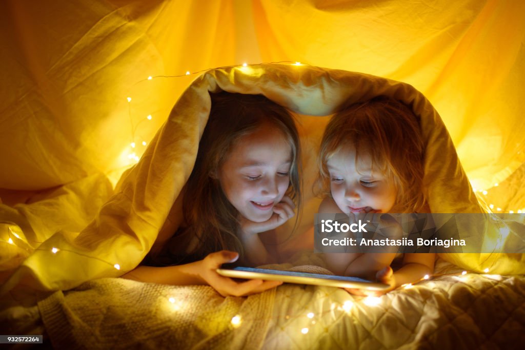 Two kids using tablet pc under blanket at night. Child Stock Photo
