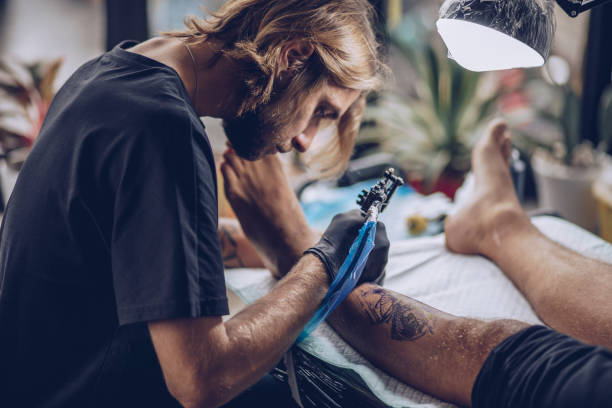 istock Young artist making tattoo on man's leg 932572698