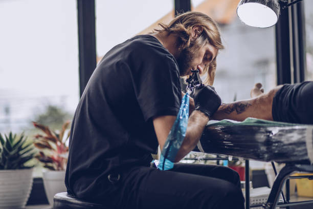 istock Young artist making tattoo on man's leg in studio 932573284