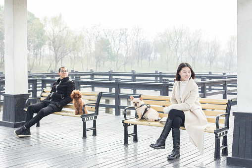 young man and woman with pets relaxing on park bench in a pavilion,China.