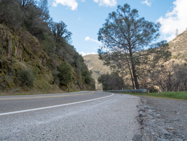 istock Low Angle View of Road That Curves Right With Large Mountains on each Side 932577336