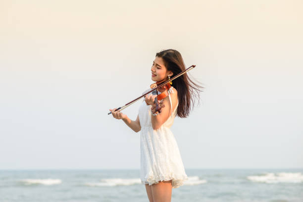 istock Happy woman playing violin on the beach. 932597360