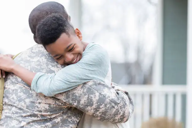 Excited African American tween boy hugs his dad as his dad returns from an overseas military deployment.