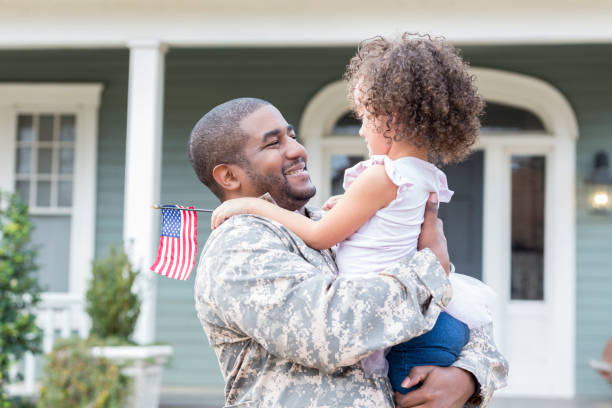 African American soldier returns from overseas Happy mid adult African American soldier picks up his preschool age daughter as he returns home from assignment. camouflage clothing photos stock pictures, royalty-free photos & images