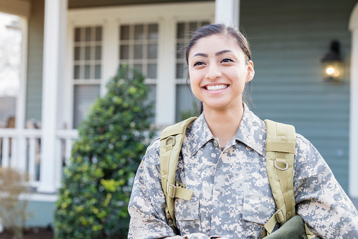 Happy young Hispanic female soldier is excited for her first deployment. Her house is in the background as she walks away.