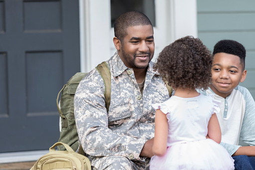 Caring soldier talks with his daughter and son before leaving for assignment. They are sitting on the front porch of their home.