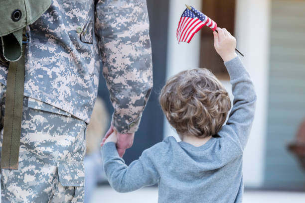 Rear view of boy holding hands with military dad Rear view of preschool age boy holding his army dad's hand. They are walking toward their home. The boy is holding an American flag. military lifestyle stock pictures, royalty-free photos & images