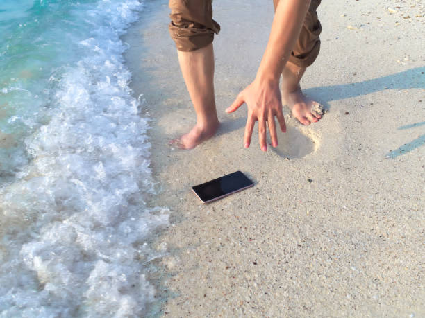 Hands of young Asian man dropping mobile smart phone on tropical sandy beach. Accident and insurance electronic equipment concept Hands of young Asian man dropping mobile smart phone on tropical sandy beach. Accident and insurance electronic equipment concept splash screen stock pictures, royalty-free photos & images