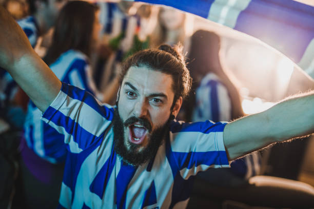 istock Young man shouting and cheering for his favorite soccer team while watching a match on TV in the living room. 932613538