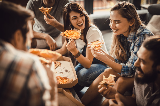 Group of happy roommates having fun while eating pizza for lunch in the living room.