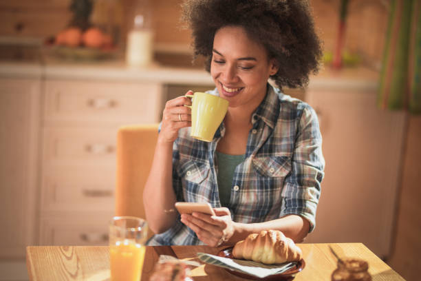 istock Happy African American woman using cell phone during coffee time at home. 932647172
