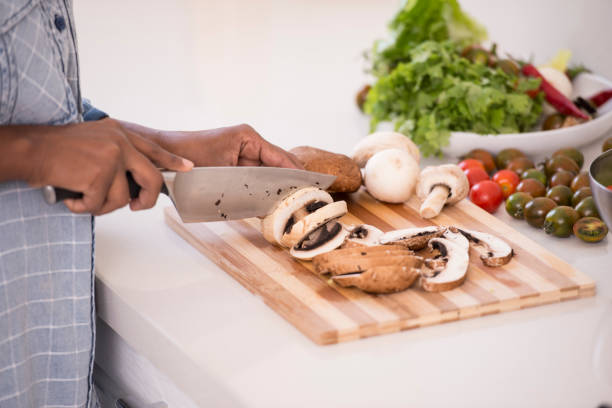 Unrecognized woman preparing fresh salad, chopping mushroom, cherry tomato, and lettuce.