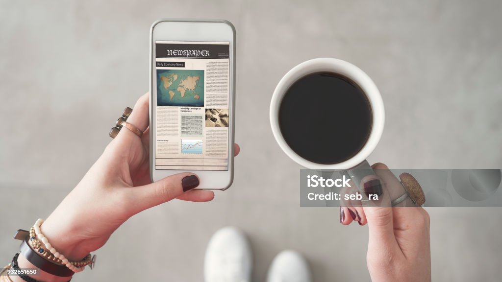 Mujer sosteniendo teléfono móvil y leer noticias en pantalla otra mano sostiene la taza de café - Foto de stock de Periódico libre de derechos