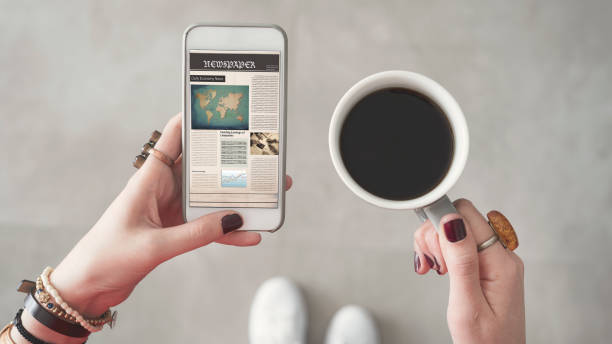 mujer sosteniendo teléfono móvil y leer noticias en pantalla otra mano sostiene la taza de café - mujer leyendo periodico fotografías e imágenes de stock