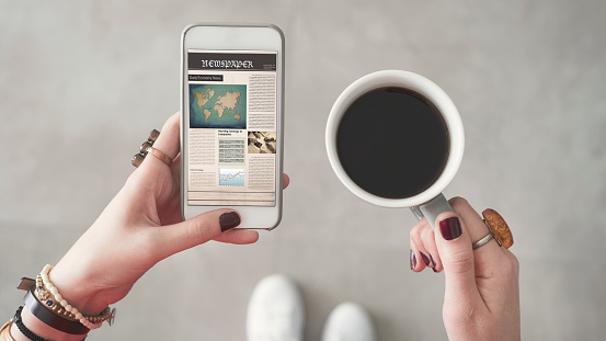 Woman holding mobile phone and reading news from screen other hand holding coffee cup