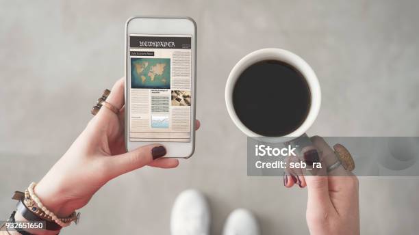 Woman Holding Mobile Phone And Reading News From Screen Other Hand Holding Coffee Cup Stock Photo - Download Image Now