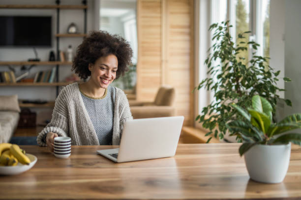 istock Young African American woman drinking coffee and using laptop at home. 932654864