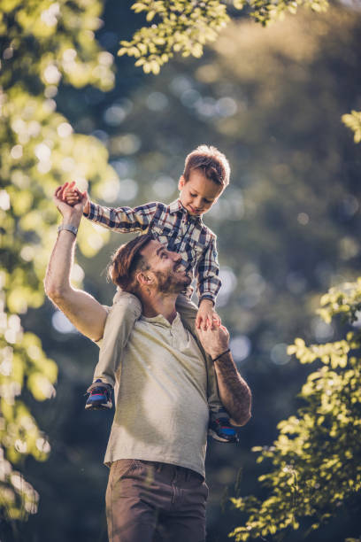 istock Young carefree father having fun while carrying his small son on shoulders in nature. 932664328