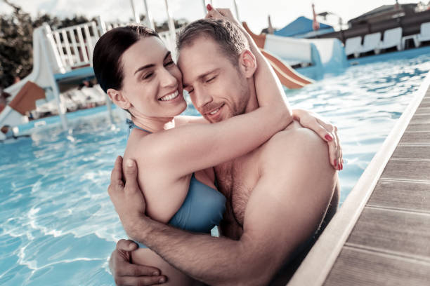istock Adorable millennial couple hugging and smiling in swimming pool 932671664