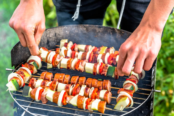 asar los alimentos sobre la parrilla de la barbacoa en el jardín de verano, las manos del cocinero preparando brochetas con verduras y carne, fiesta al aire libre con barbacoa en pasto - grilled broiling outdoors horizontal fotografías e imágenes de stock