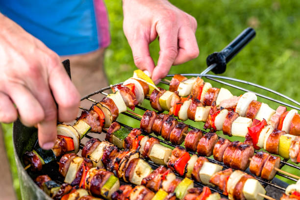 grelhar alimentos na churrasqueira, mãos a preparação dos espetos com legumes e salsicha, festa ao ar livre com churrasco na grama - barbecue grill broiling barbecue vegetable - fotografias e filmes do acervo