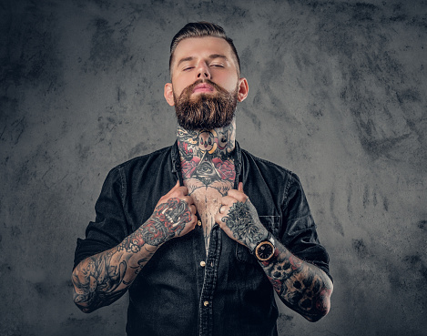 Studio portrait of bearded hipster man with tattoos on his arms, chest and neck.