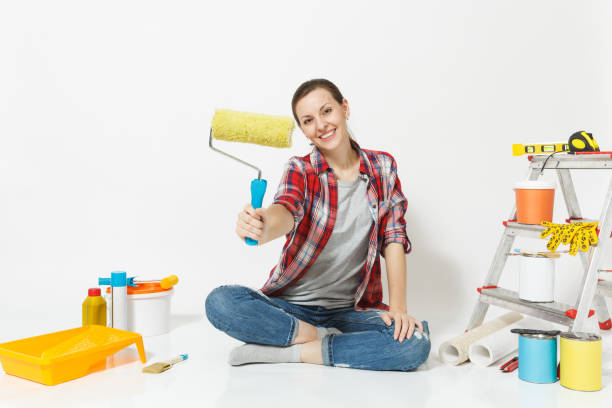 istock Woman in casual clothes sitting on floor with paint roller, instruments for renovation apartment isolated on white background. Wallpaper, accessories for gluing, painting tools. Repair home concept. 932709128