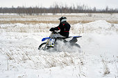 Sportsman racer man fulfills a fast ride on a motorcycle on the road extreme. The race track is very uneven. Cloudy winter day with a snowstorm.