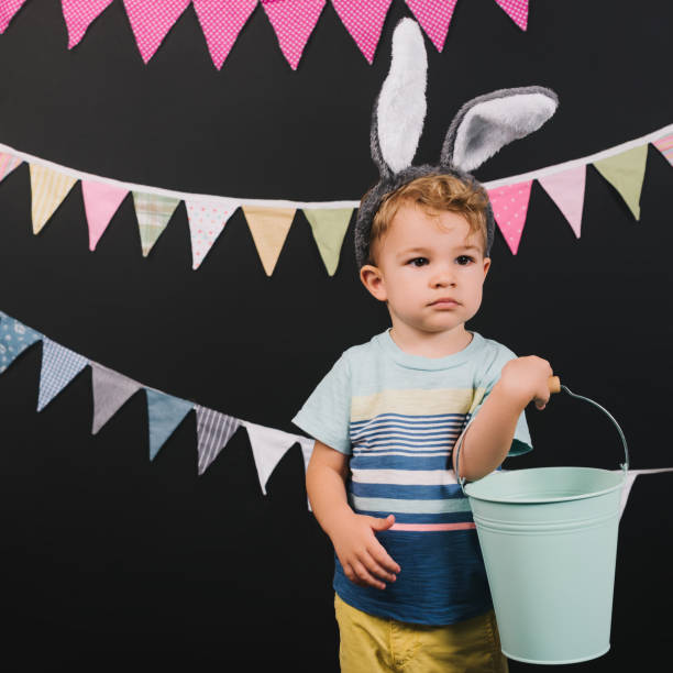 istock adorable little kid with bunny ears and bucket on black, easter concept 932723166