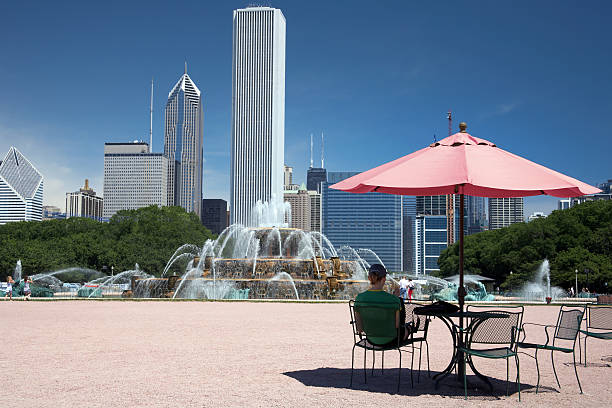 Buckingham Fountain Girl sitting in the shade of a cafe umbrella near Chicago's Buckingham fountain grant park stock pictures, royalty-free photos & images