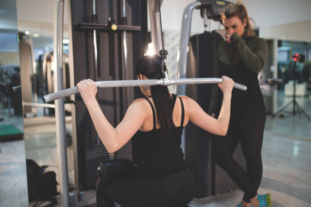 istock Young Woman Working Out On Lat Machine with Assistance Of Instructor 932747360