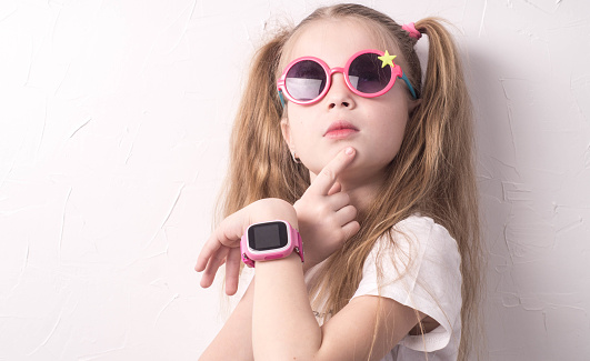 Technology for children: a girl wearing pink glasses uses a smartwatch. Portrait.