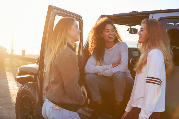 tres jóvenes amigas en un viaje por carretera hablando al lado de coche - face to face twilight togetherness vertical fotografías e imágenes de stock