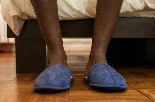 Mid adult African businessman waking up in the morning slipping his slippers on.