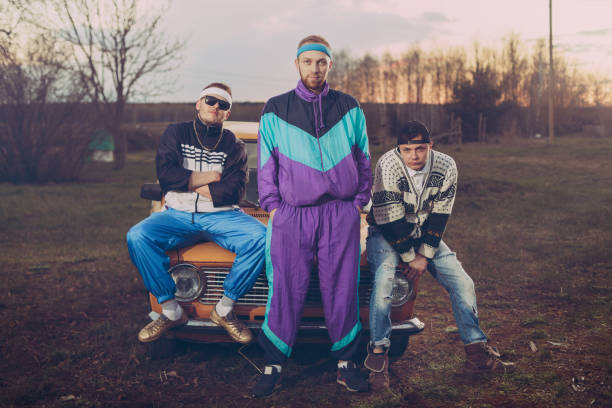 tres amigos en el estilo de los años noventa son naranja coche viejo, - vintage attire fotografías e imágenes de stock