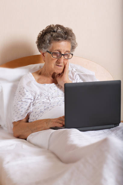 старшая женщина использует свой ноутбук, находясь в постели - respect women human teeth people стоковые фото и изображения