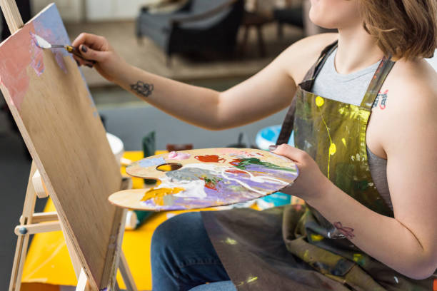 istock Young inspired girl applying primer on canvas in light studio 932757824