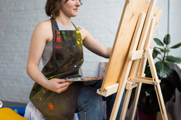 istock Young artistic girl painting on canvas in light studio 932758802