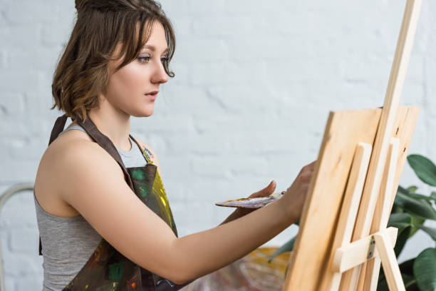 istock Young inspired girl working by easel in light studio 932758894