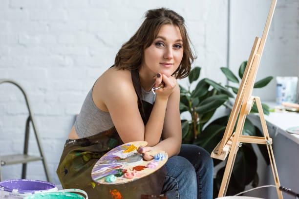 Young artistic girl with hand on chin looking at camera in light studio