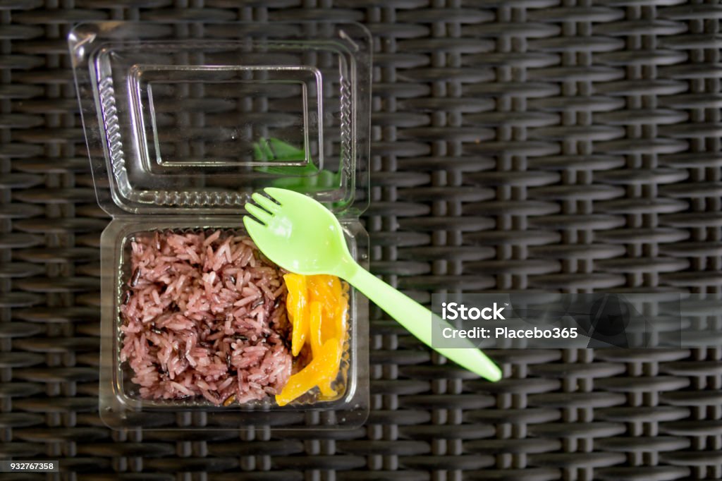 Plastic container with Thai Breakfast sweet Mango sticky rice (Kao Niaw Mamuang) This is a traditional Thai street food dish.  Sweet Sticky rice with Mango, aka Kao Niaw Mamuang.  In a plastic take away container with plastic fork.  The food is arranged in the ‘knolling’ style on a plain background.  Image taken in studio in Thailand. Plastic Cutlery Stock Photo