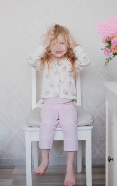 Photo of little girl blonde sitting on a chair in her pink pajama top, causing chaos on the head
