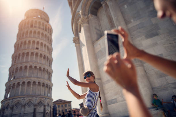 holding up photos of the Leaning Tower of Pisa Family sightseeing Pisa, Italy. Teenage girl is posing by the leaning tower of Pisa.  Mother is taking photos and the bored boys are fighting in the background.
Kids are aged 8 and 11.
Nikon D810 city break photos stock pictures, royalty-free photos & images