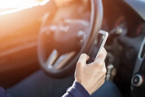 Woman driving car and texting message on smartphone
