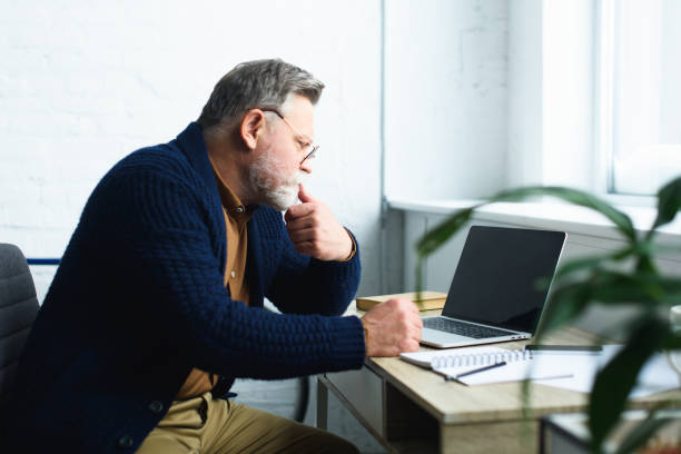 istock side view of focused senior man in eyeglasses using laptop with blank screen 932786248