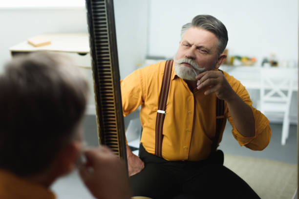 istock handsome bearded senior man trimming moustache with scissors and looking at mirror 932786778